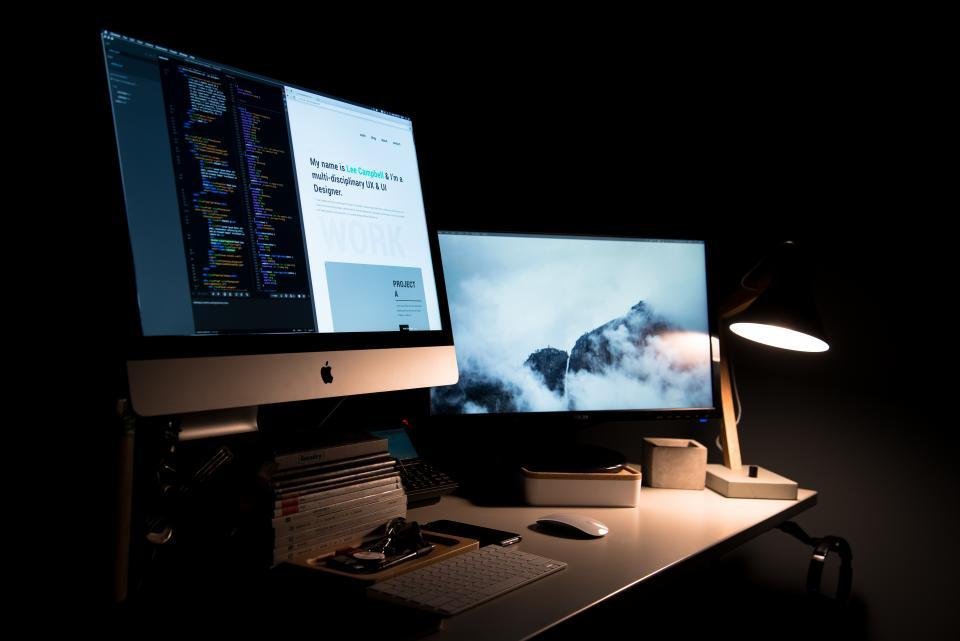 A desk with two monitors side by side lit by a lamp