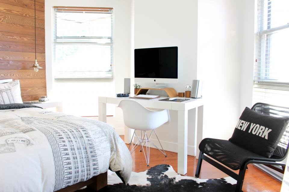 A compact white desk with a molded shell chair against a wood-panelled wall in a light-filled room