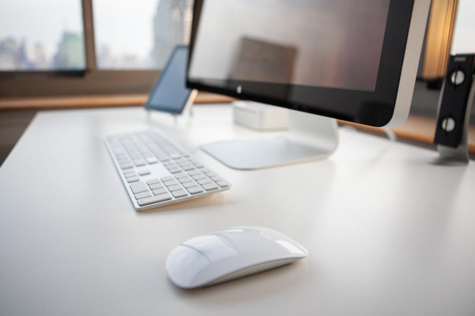 A minimalist white desk with an all-in-one computer, small plant and tidy accessories