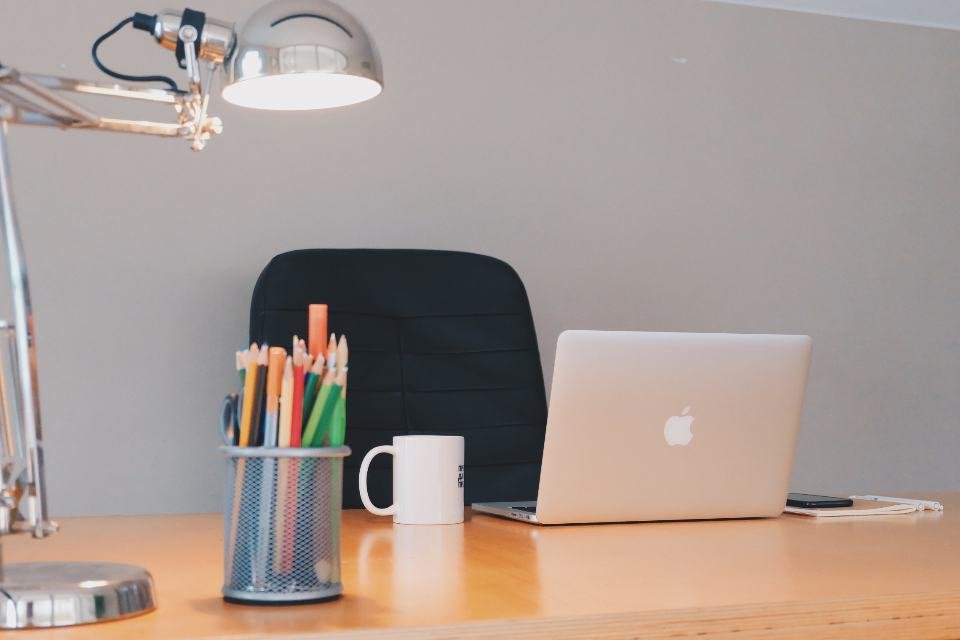 A black office chair at a wooden desk with a lamp