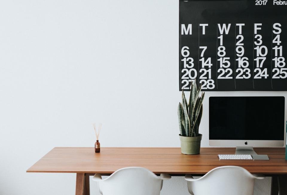 A tidy wooden desk with a computer, plant and wall calendar