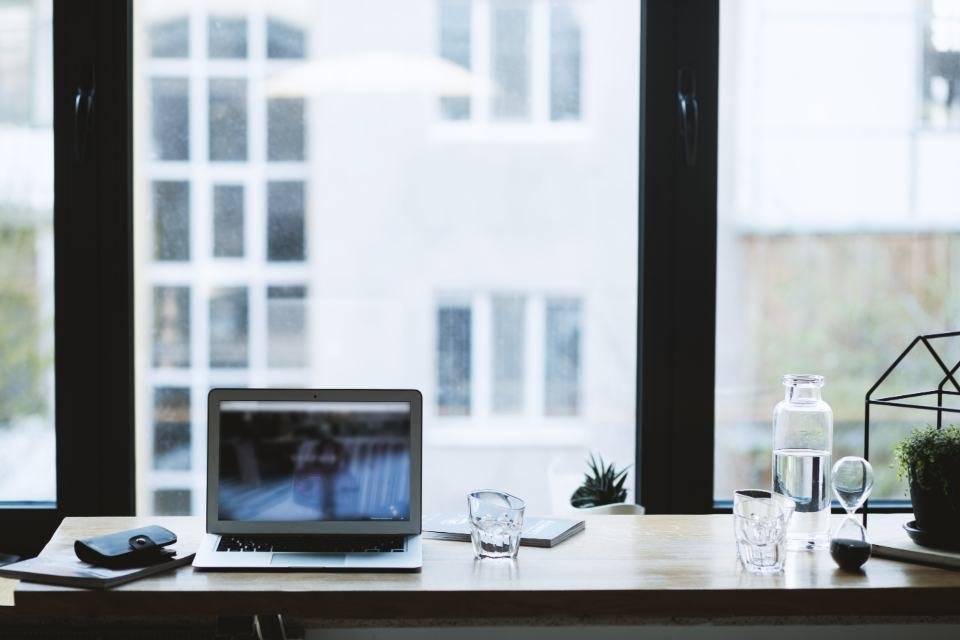 A laptop on a desk in front of a large window with a plant